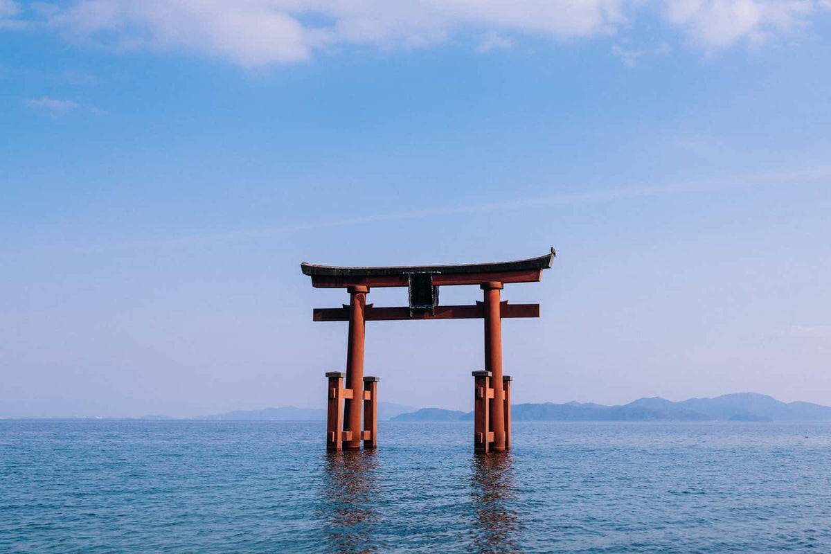 Torii gate standing in water with mountains in the background under a clear blue sky.