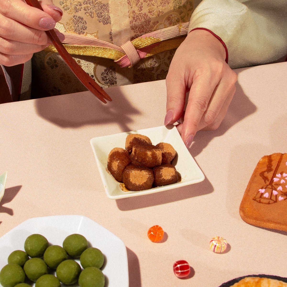 Person in traditional Japanese attire holding chopsticks over a plate of kinako-covered mochi.
