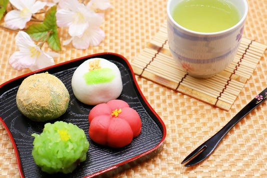 A plate of traditional Japanese sweets (wagashi) served with green tea and cherry blossoms in the background.