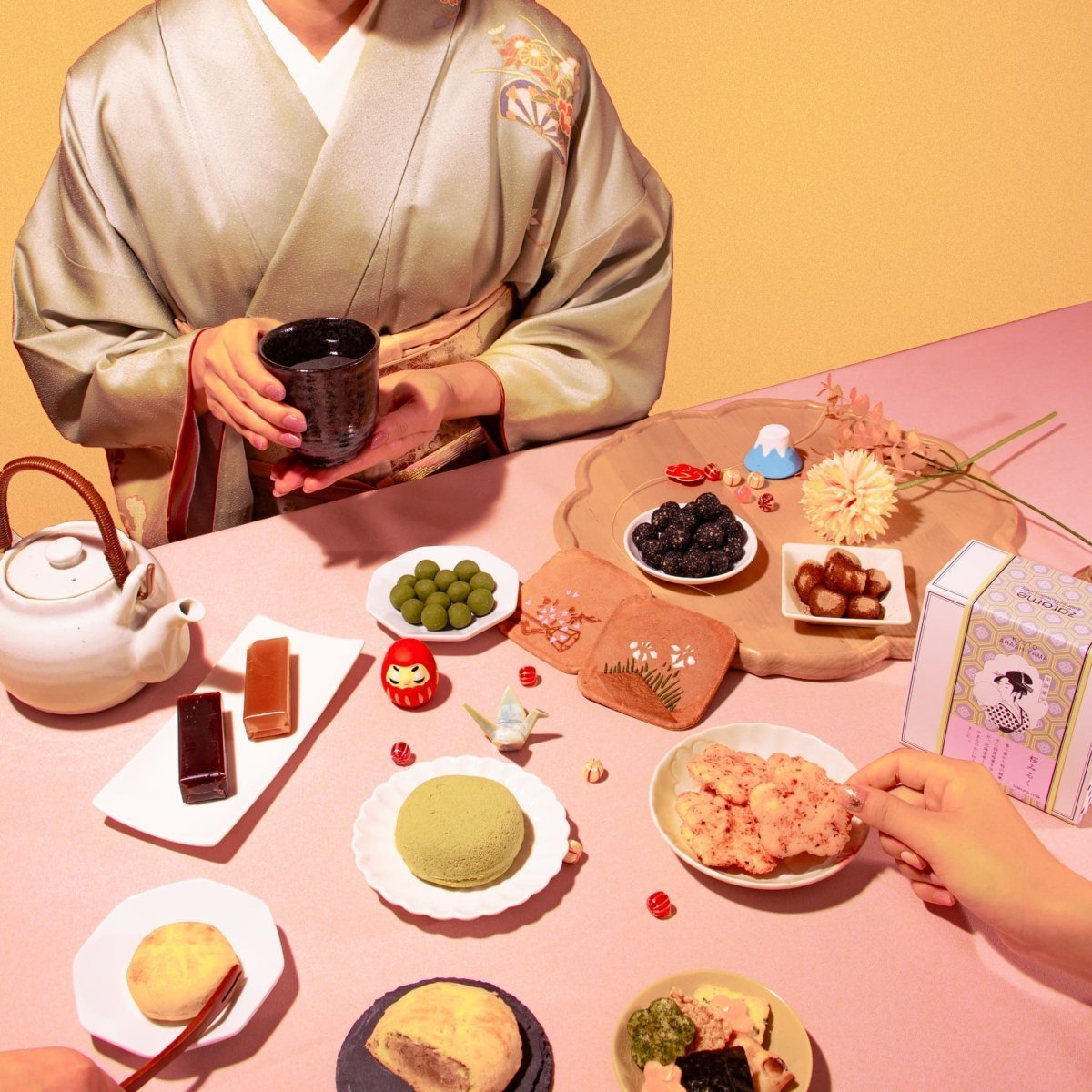 Woman in a traditional Japanese kimono enjoying a tea ceremony with various Japanese sweets and snacks arranged on a table, including mochi, rice crackers, and sweets, against a pink and yellow background.